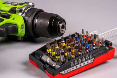 Düz bir yüzey üzerinde ev onarımı çalışmaları için çeşitli tornavida parçaları ve aksesuarları içeren bir alet setinin yanına bir elektrikli matkap yerleştirilir.