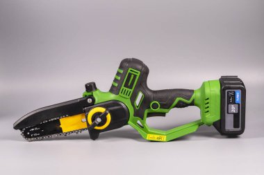 Bir insan elinde küçük bir pil motorlu testere tutar. Elektrikli testere dalları budamak için ve bahçe işlerinde kullanılır..