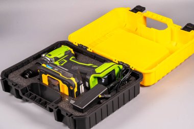 Kablosuz matkap, içi siyah olan sarı bir çantanın içinde duruyor. Matkap şarj cihazının ve aksesuarlarının yanında, ev projelerinde veya onarımlarda kullanılmaya hazır..