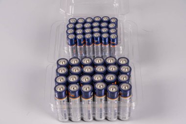 Temiz plastik bir kabın içinde düzenlenmiş bir pil koleksiyonu beyaz bir yüzey üzerinde bulunur. Piller yeni ve çeşitli cihazlarda kullanıma hazır..