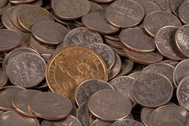 Birçok madeni para düz bir yüzeyde yatıyor. Çoğu gümüş, ama biri altın ve göze çarpıyor. Bozuk paraların boyutları ve tasarımı farklıdır, karışık bir yığın oluşturur..