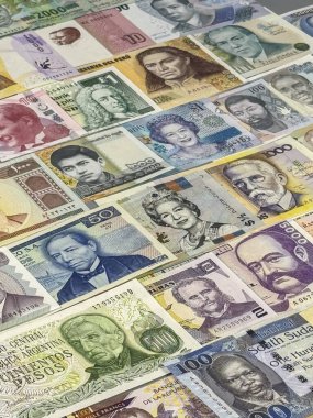 Birçok ülkeden gelen renkli banknotların bir koleksiyonu düz bir yüzeye yayılır. Her notada eşsiz dizaynlar, sayılar ve resimler var..