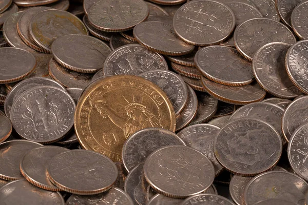 Birçok madeni para düz bir yüzeyde yatıyor. Çoğu gümüş, ama biri altın ve göze çarpıyor. Bozuk paraların boyutları ve tasarımı farklıdır, karışık bir yığın oluşturur..