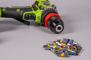 Gri bir yüzeye matkap ucu koleksiyonunun yanına bir elektrikli matkap yerleştirilir. Matkabın siyah ve yeşil bir tasarımı var. Parçalar farklı renklerde düzenlenmiş..