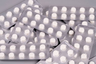 Birden fazla beyaz hap paketi gri bir yüzeyde rastgele bir düzende düzenlenir. Paketler mühürlü ve sıra sıra yuvarlak tabletleri gösteriyor. Ayar herhangi bir belirgin özelliğe sahip değil.
