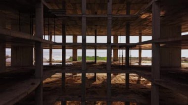 Tepeden çekilen çekim, beton kirişlerle tamamlanmamış bir binayı yakalıyor. Kıyı manzarası açık alanlarından görülebiliyor ve doğal bir zemin ortaya çıkıyor..