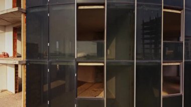 Hava manzarası, cam cepheli bir inşaat alanı yakalıyor. Çevredeki yapılar görülebiliyor ve gün ışığında tamamlanmamış bir şehir manzarasını ortaya çıkarıyor..