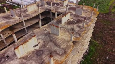 Paslanmış inşaat demirleri ve beton yapıları olan terk edilmiş bir inşaat alanının havadan görüntüsü. Çevredeki bitki örtüsü, bölgenin ıssızlığıyla tezat oluşturarak vahşileşiyor..