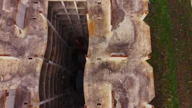 Havadan bakıldığında yıkık dökük duvarları ve merkezinde açık bir alanı olan harap bir inşaat alanı görülüyor. Terk edilmiş yapıyı çevreleyen yeşil çimenler.