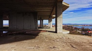 Hava görüntüsü, beton sütunlarla terk edilmiş bir yapının içini yakalar. Manzara, temiz bir gökyüzünün altında nehir kenarı ve tepeleri ortaya çıkarıyor..