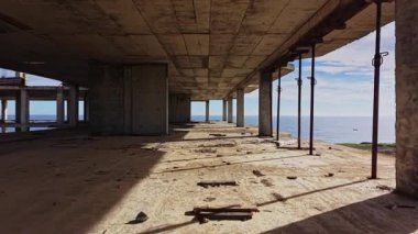 Terk edilmiş bir sahil binasının içi. Güneş ışığı açık alanlardan akar, beton zeminde uzun gölgeler bırakır..
