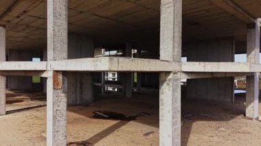 Terk edilmiş bir binanın tamamlanmamış yapısını görüntüleyen hava manzarası, tenha bir arazide gün ışığında beton sütunlar ve boş iç mekanlar ortaya çıkarıyor..