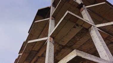 İnşaat sahasında, gün ışığında berrak bir gökyüzüne karşı ham endüstriyel yapıyı gösteren açık kirişli bitmemiş beton bir bina bulunuyor..