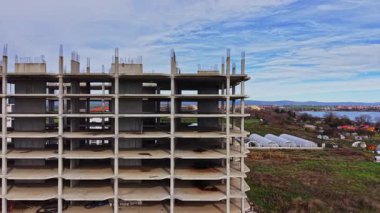 Bereketli yeşilliklerin ve açık mavi gökyüzünün altındaki suyun ortasındaki kısmen inşa edilmiş bir yapıdan beton sütunlar yükseliyor..