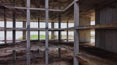 Hava görüntüsü, sahil kenarındaki tamamlanmamış beton bir binanın iskelet kalıntılarını gösteriyor. Doğa alanı geri almaya başlıyor, kentsel bozulmayı vurguluyor ve ihmal ediyor.