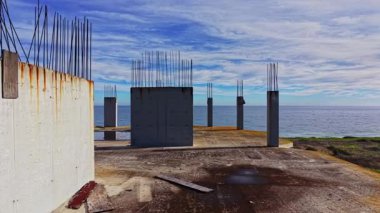 Suyla ve mavi gökyüzüyle çevrili bir kıyı şeridinde beton tezgahı olan beton temeller, kıyı şeridinde devam eden inşaat çalışmalarını akla getiriyor..