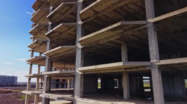 Hava görüntüsü, açık gökyüzünün altında bir inşaat alanının beton iskeletini yakalıyor. Çevre bölgeler eksik yapıları ve açık araziyi gösteriyor.
