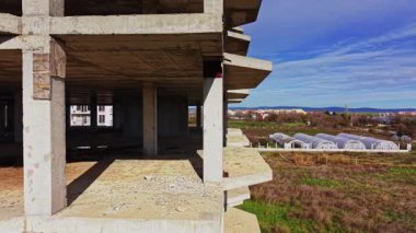 Yukarıdan bakıldığında seralar ve açık alanların yanında tamamlanmamış beton bir yapı görülüyor. Manzara geniş, kentsel ve kırsal ortamların bir karışımı olduğunu gösteriyor..