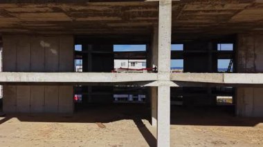 Bu hava manzarası, beton sütunlarını ve açık alanlarını vurgulayan gelişmekte olan bir binanın iskeletini gösteriyor. İşçiler inşaata hazırlanırken görülebilir.