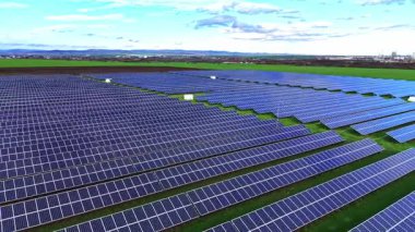 Yeşil arazi boyunca uzanan güneş panelleri yenilenebilir enerji çözümleri sergiliyor. Sahne bulutsuz, aydınlık bir günde çekiliyor..