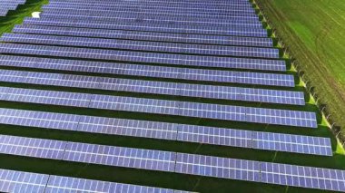 Güneş panellerinin sıraları yeşil bir alan boyunca uzanıyor ve güneş ışığını etkili bir şekilde yakalıyor. Bu hava görüntüsü, yenilenebilir enerjinin arazi üzerindeki artan etkisini vurgular..