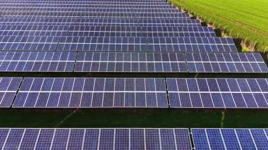 Yeşil alana yerleştirilmiş büyük bir güneş paneli enerji üretimi için güneş ışığını yakalıyor. Hava görünümü, panellerin organize sıralarını ve etrafındaki çimenleri vurgular.