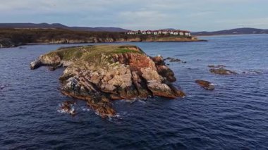 Hava perspektifi, sakin sularla çevrili engebeli kayalık bir adayı yakalar. Uzak evler kıyı şeridinde oturur, huzurlu manzarayı güzelleştirir..
