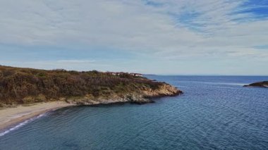 Bu hava manzarası sakin suları ve kıyı şeridi boyunca yemyeşil suları olan sakin bir sahili yakalar. Bulutlu gökyüzü okyanus kenarında huzurlu bir öğleden sonrayı yansıtıyor..