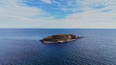 Sahne, parlak bir gökyüzünün altında sakin ve mavi sularla çevrili küçük bir adayı yakalıyor. Bereketli yeşillik kayalık karada görülebilir, sakin bir atmosfer yaratır..