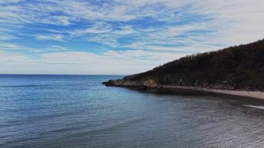 Bu hava manzarası, sakin bir kıyı şeridini ve mavi gökyüzünün altındaki sakin suları yansıtıyor, sakin bir çevrede doğanın güzelliğini gösteriyor..