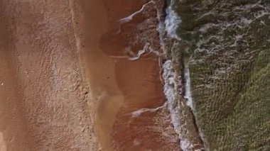 Yukarıdan bakıldığında, kıyı şeridi kumsalda güneşli bir günde yumuşak kum dalgalarıyla karşılaşıyor, birbirini nazikçe yuvarlıyor..