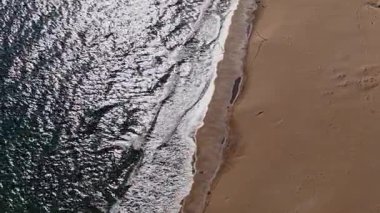 Bu hava görüntüsü, okyanus dalgaları ve kumlu sahil arasındaki güzel etkileşimi yakalar. Gün ortasındaki renk ve dokuların kontrastını vurgular..