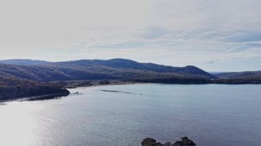 Bu hava manzarası, berrak bir gökyüzünün altında yemyeşil tepeler ve uzak dağlarla çevrili sakin sularla dolu huzurlu bir koy sergiliyor..