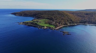Geniş mavi sular yemyeşil bir yarımadanın etrafını sarar, berrak bir gökyüzü altında sakin bir kıyı manzarası sergiler, doğa severler ve açık hava aktiviteleri için mükemmeldir..