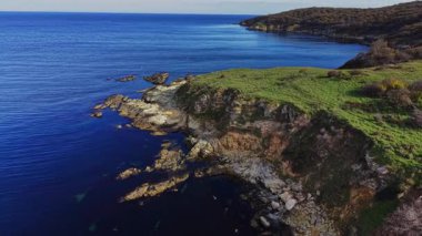 Dalgalar, güneş doğarken engebeli uçurumlara hafifçe çarparak huzurlu manzarayı aydınlatıyor. Sakin sular sabahın ilk ışıklarını yansıtarak huzur verici bir manzara yaratıyor..
