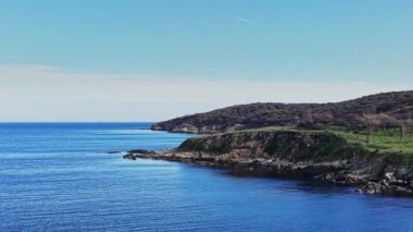 Havadan bakıldığında engebeli kıyı kayalıklarının berrak mavi denizle buluşması görülüyor. Sakin sular, doğanın güzelliğini ve sükunetini gösteren barışçıl bir atmosferi yansıtıyor..