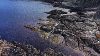 Bu hava manzarası kıyı şeridi boyunca engebeli kayaları ve nazik dalgaları yakalar. Su, yumuşak sabah ışığını yansıtır ve sakin bir atmosfer yaratır..