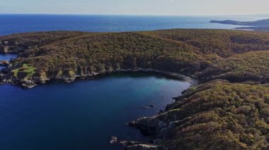 Bu sahne, berrak mavi suları ve canlı yeşillikleri olan güzel bir sahil şeridini gösteriyor. Hava perspektifi bölgenin doğal güzelliğini gözler önüne seriyor..