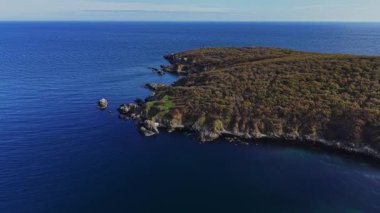Kıyı şeridinde kayalık çıkıntıları çevreleyen berrak mavi suyla ağaçlarla kaplı dik uçurumlar yer alıyor. Bu çarpıcı manzara doğanın güzelliğini gözler önüne seriyor..