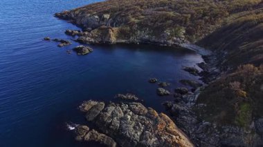 Bu hava görüntüsü engebeli bir kıyı şeridini koyu kayalar ve berrak mavi sularla yakalıyor. Bereketli yeşillik kıyı şeridi oluşturur, sakin ve manzaralı bir manzara yaratır..