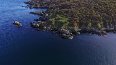 Bu hava manzarasında kayalık bir kıyı şeridi, yemyeşil alanlar ve koyu mavi sulardan oluşan sakin bir kıyı manzarası sergilenmektedir. Doğanın güzelliği mükemmel bir şekilde yansıtılır..