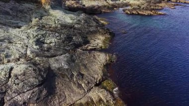 Hava sahnesi, dokulu kayalar ve derin mavi sularla engebeli bir kıyı şeridi yakalıyor. Güneş batıyor, yeryüzüne sıcak bir ışık saçıyor, sakin bir atmosfer yaratıyor..