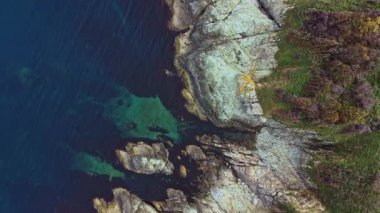 Hava manzarası, berrak mavi suları çevreleyen engebeli kıyı kayalıklarını yakalar. Canlı doğal renkler gün ışığında bu dingin manzaranın güzelliğini gösteriyor..
