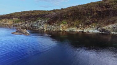 Sahne kayalık uçurumlar ve sakin mavi sularla sakin bir sahil şeridi yakalıyor. Yeşil ağaçlar bu huzurlu doğal ortamda temiz bir gökyüzünün altındaki manzarayı süslüyor..