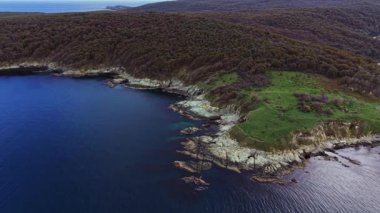 Bu hava görüntülerinde kayalık bir kıyı şeridine ulaşan yuvarlanan yeşil tepelerin yer aldığı güzel bir kıyı bölgesi görülüyor. Sakin mavi su huzurlu atmosferi güçlendirir..