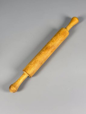 Ahşap bir oklava gri bir yüzeyde duruyor. Pişirme işlerinde hamuru düzleştirmek ve yemek pişirmek için gerekli aletleri vurgulamak için kullanılır..