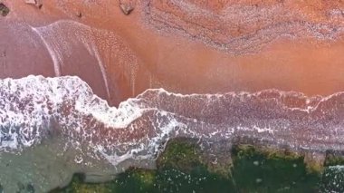 Bu güzel hava manzarası kumlu bir kıyıya vuran yumuşak dalgaları yakalar, güneşli bir günde deniz ve kumdaki desenleri ve renkleri ortaya çıkarır..
