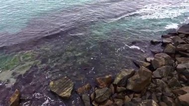 Yukarıdan, turkuaz sular, deniz ve karanın zıtlığını gösteren kayalık kıyılarla nazikçe buluşur. Sahne, kıyı manzarasının güzelliğini canlı detaylarla yakalıyor..