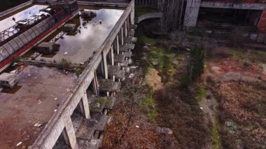 Yoğun aşırı büyümeyle çevrili harap olmuş bir endüstriyel kompleksin havadan görünüşü. Doğa alanı geri alırken, binanın düz çatılarında su birikiyor..