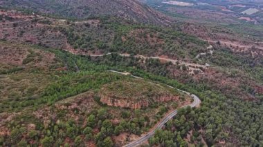 Virajlı yol İspanya 'nın kırsal kesimindeki yeşil tepeleri ve ağaçları kesiyor. Manzara açık mavi gökyüzünün altındaki tepeleri ve vadileri gösteriyor. Doğa yolu sarmış..